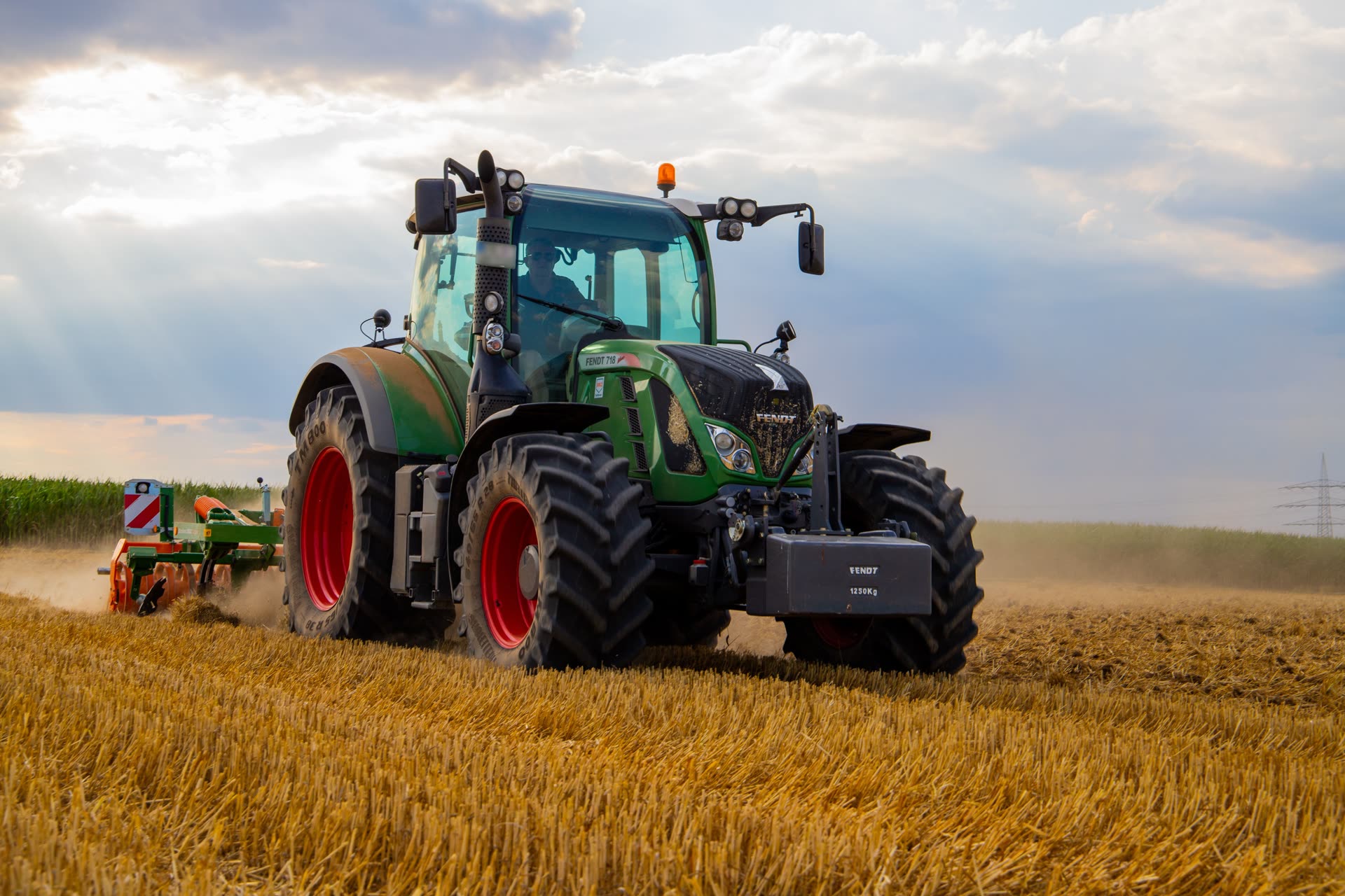 A Fendt tractor plowing a wheat field under a dramatic sky